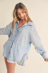 woman wearing a light blue striped oversized button-up shirt with a chest pocket and rolled-up sleeves