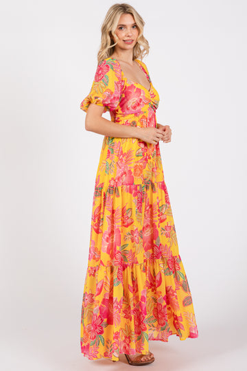 woman wearing a bright yellow floral maxi dress with puff sleeves and a tiered skirt, standing sideways