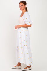 woman wearing a white floral maxi dress with puff sleeves and a smocked bodice, standing sideways against a plain background