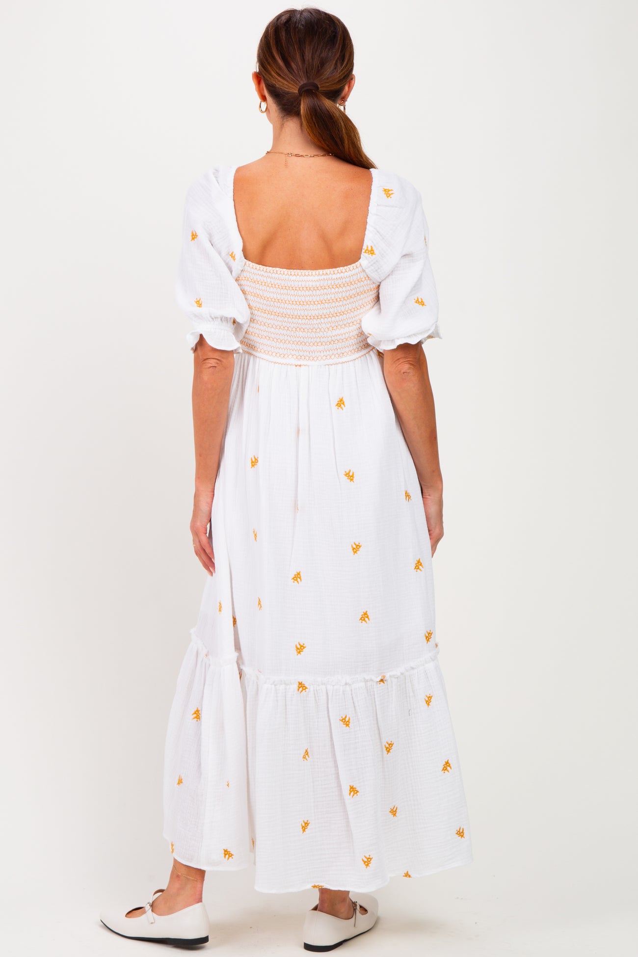 woman wearing a white maxi dress with floral embroidery and a smocked back, seen from the back