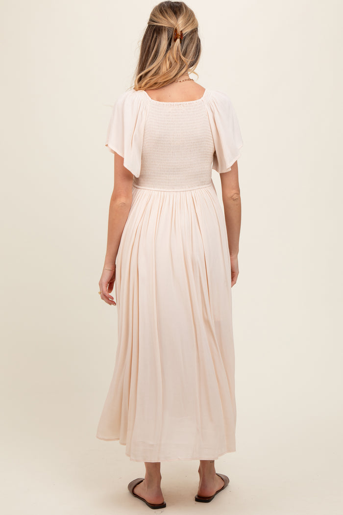 woman wearing a light pink maternity maxi dress with short flutter sleeves and a smocked bodice, showing her baby bump