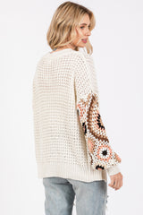 woman wearing a cream open knit sweater with patterned sleeves and distressed light blue jeans