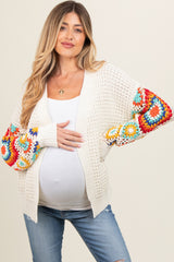 woman wearing a cream crochet maternity cardigan with colorful patterned sleeves and holding her baby bump