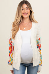 woman wearing a cream crochet maternity cardigan with colorful patterned sleeves and a visible baby bump