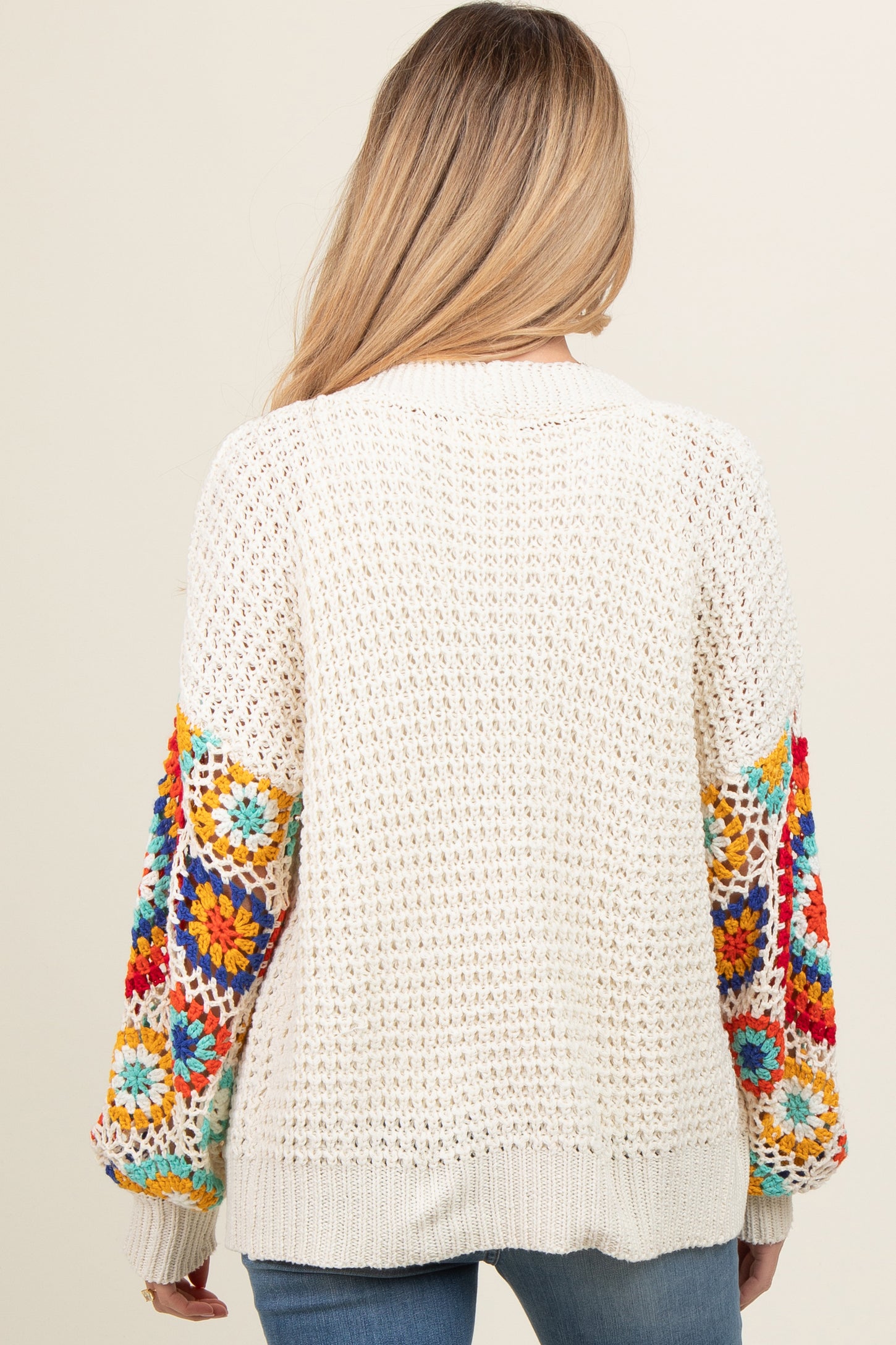 woman wearing a cream crochet maternity sweater with colorful floral patterned sleeves and a relaxed fit