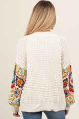 woman wearing a cream crochet maternity sweater with colorful floral patterned sleeves and a relaxed fit