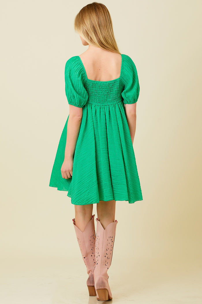 woman wearing a green smocked mini dress with puff sleeves and styled with pink knee-high boots