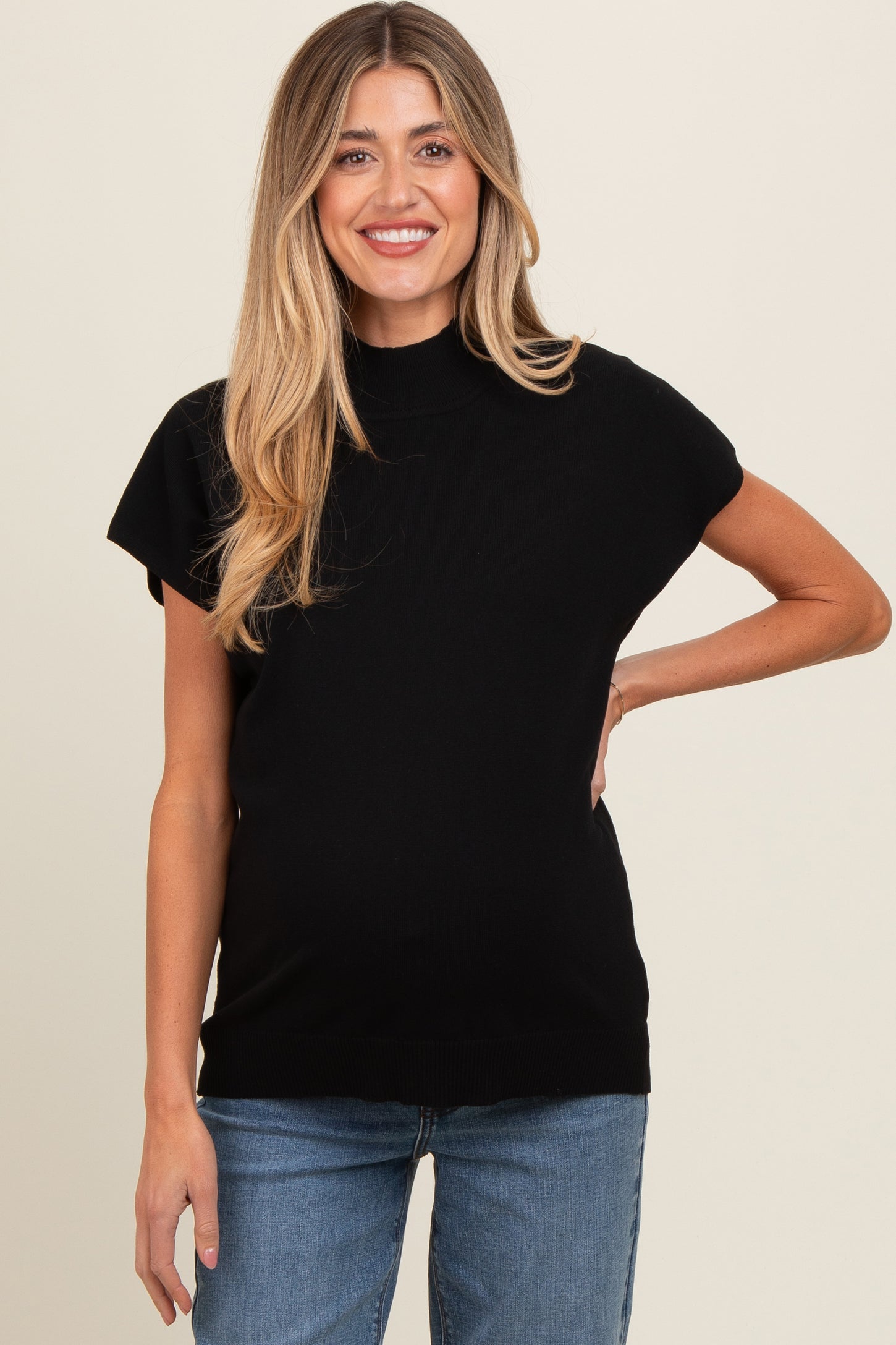 woman wearing a black short sleeve maternity top and showing her baby bump while smiling