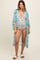 woman wearing a light blue floral maternity cover-up over a black and white polka dot swimsuit and displaying her baby bump