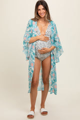 woman wearing a floral blue maternity cover-up over a black and white swimsuit, holding her baby bump
