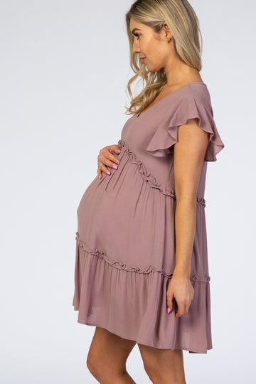 Pregnant woman in a mauve ruffled maternity dress holding her baby bump against a white background