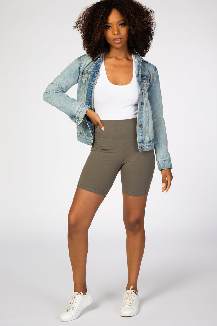 woman wearing olive green ribbed biker shorts with a white tank top and light wash denim jacket