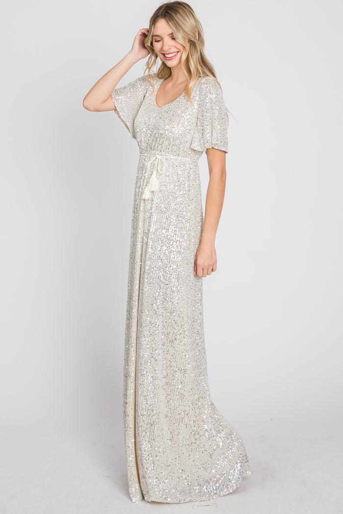 Woman wearing a white sequin maxi dress with flutter sleeves and a tassel waist tie