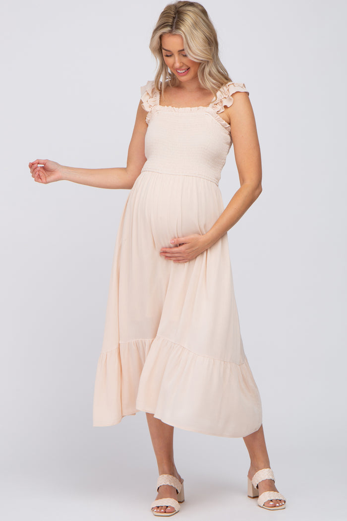 Pregnant woman in a light pink smocked maternity midi dress with ruffle straps and tiered skirt