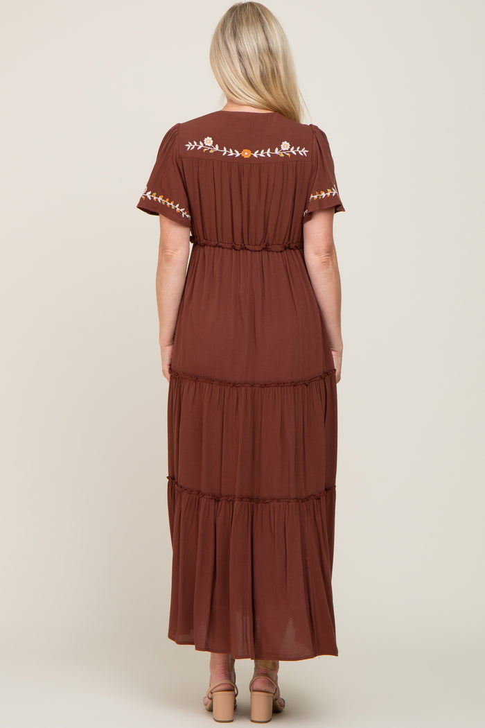 Back view of a woman wearing a brown tiered maxi dress with floral embroidery on the shoulders and back