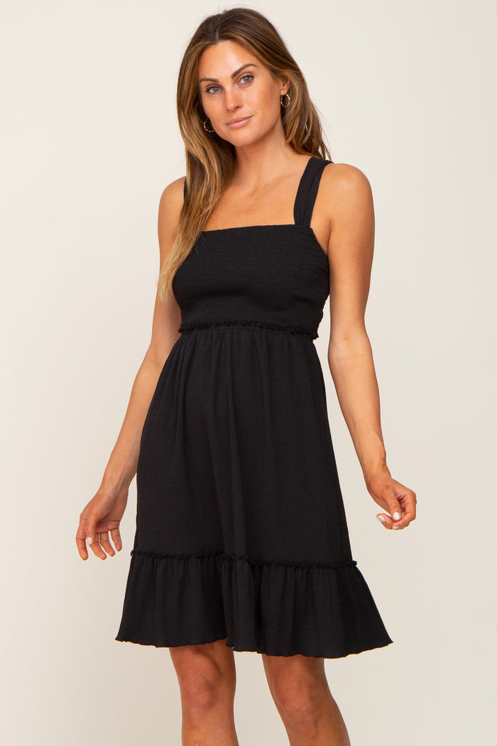 woman wearing a black smocked maternity dress with thick straps and a ruffled hem