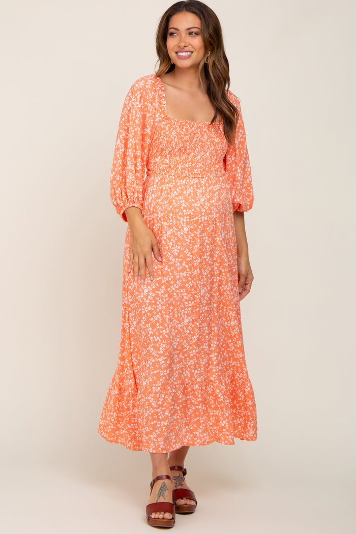 smiling woman wearing orange floral smocked maternity midi dress with puff sleeves