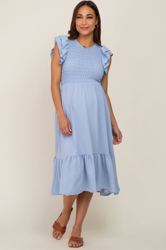 Pregnant woman wearing a light blue smocked maternity midi dress with ruffle sleeves and brown sandals