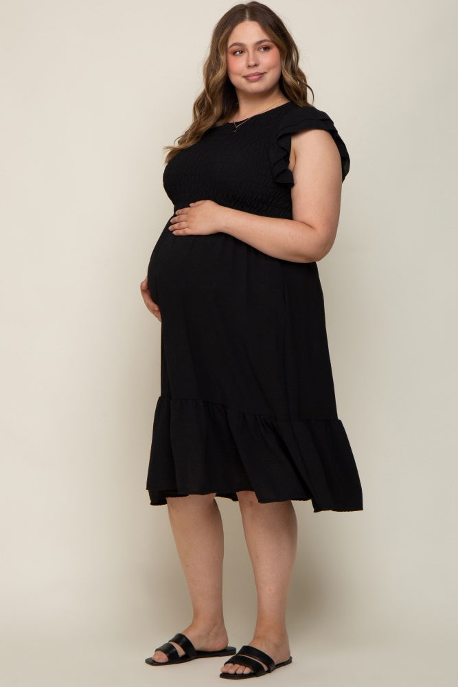 Pregnant woman wearing a black smocked maternity dress with ruffle sleeves and a tiered hem