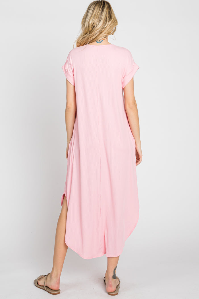 Back view of a woman wearing a light pink short sleeve ribbed midi dress with side slits and a curved hem