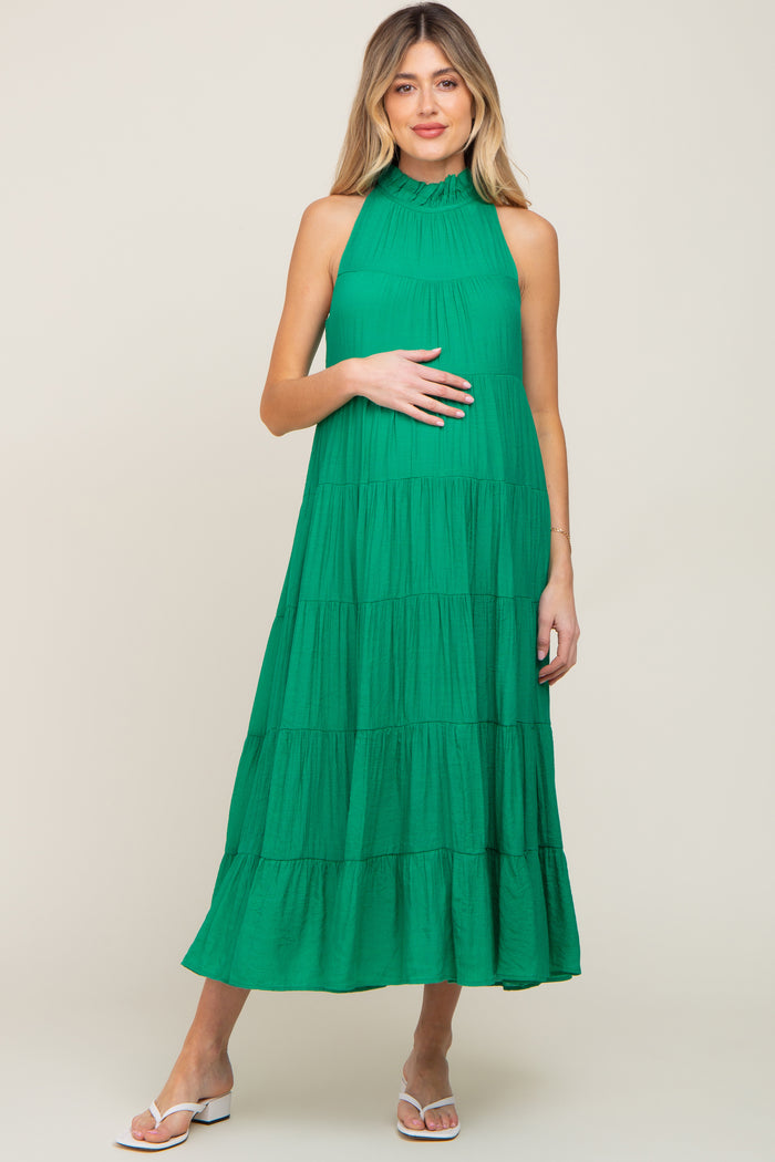 woman wearing a green tiered maternity maxi dress with a high ruffled neckline and white sandals