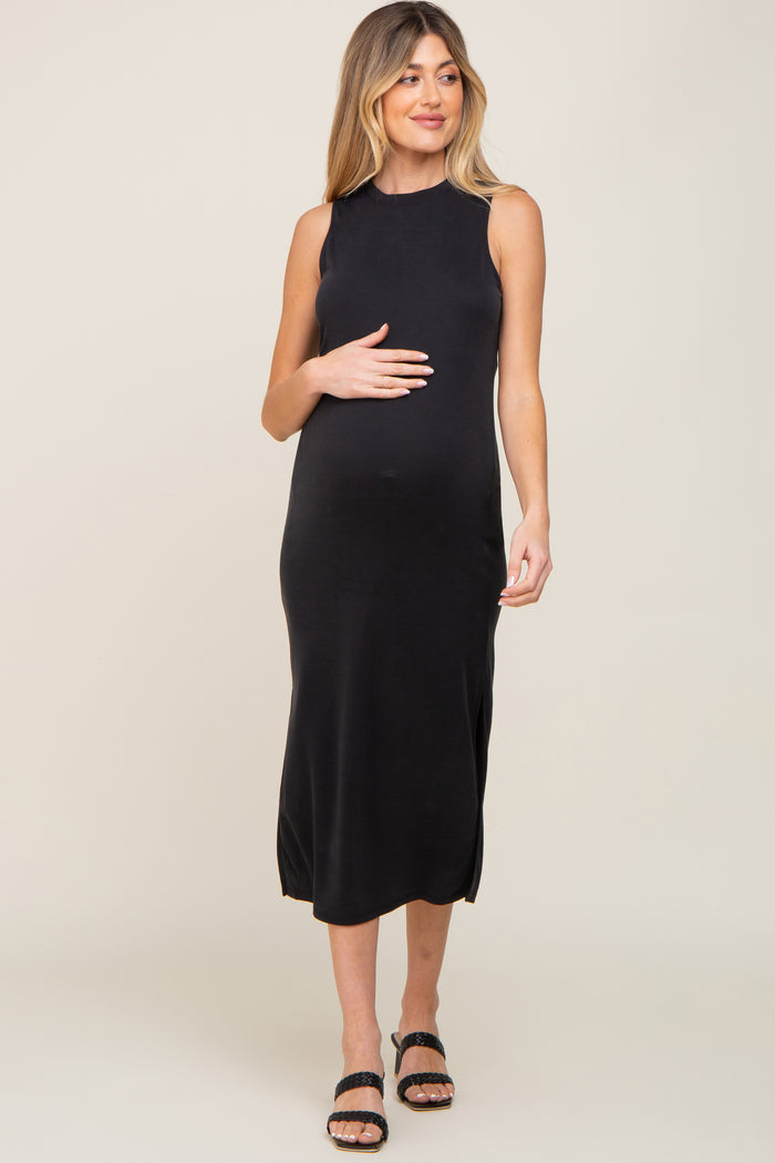 Pregnant woman wearing a sleeveless black midi maternity dress and black sandals