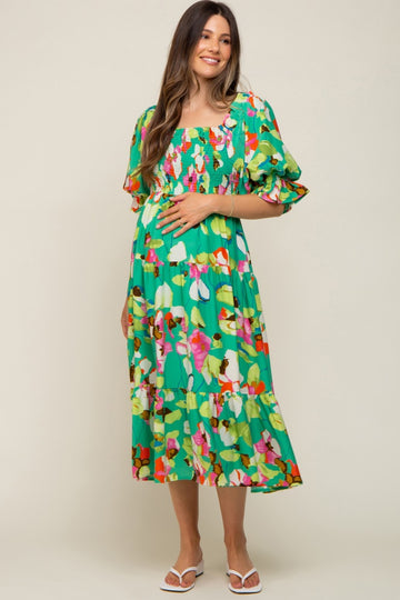 woman wearing a vibrant green floral maternity dress with puff sleeves and a baby bump visible