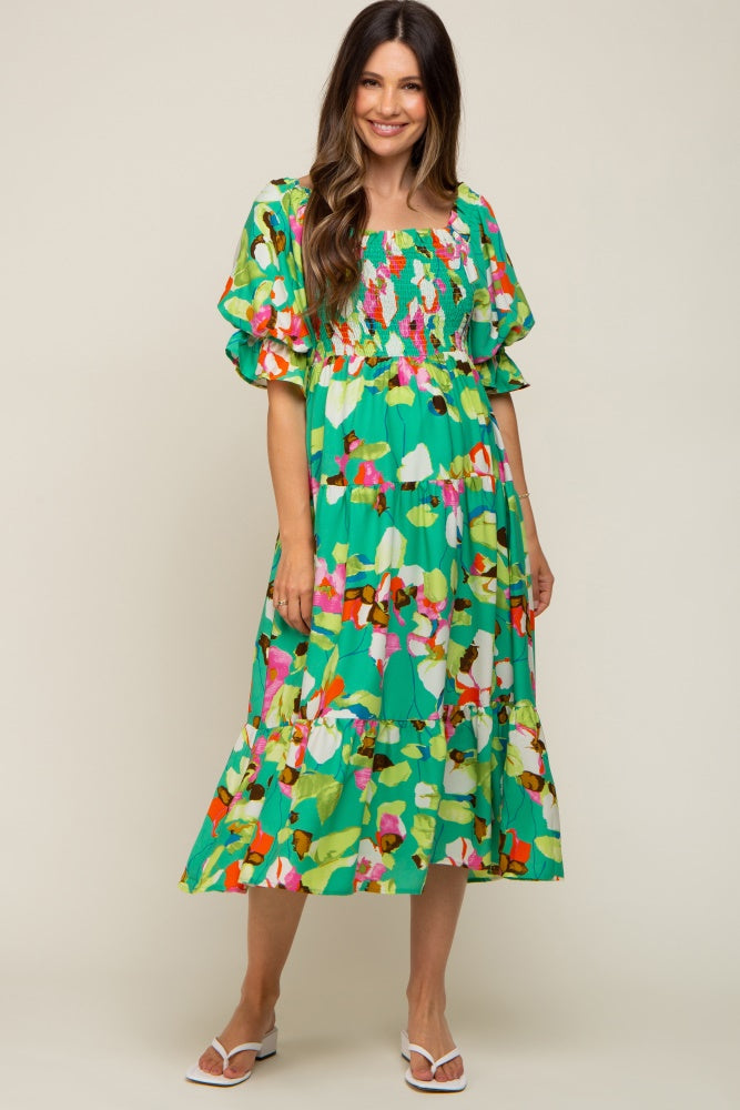 woman wearing a vibrant green floral maternity dress with puff sleeves and a tiered skirt, showcasing a baby bump