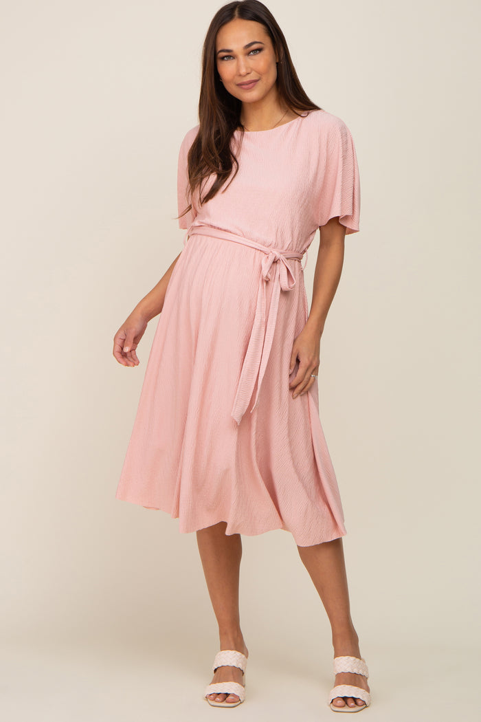 woman wearing a light pink short sleeve maternity midi dress with a waist tie and pleated texture